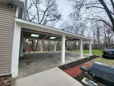 Covered carport with white columns over a concrete slab beside a house