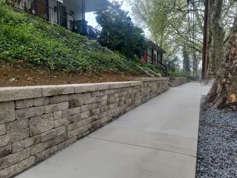 Block retaining wall along a concrete sidewalk below a planted slope