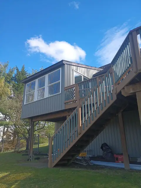 Raised sunroom addition over deck stairs, with gray siding