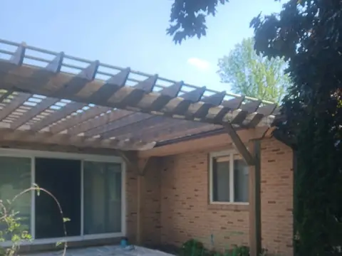 Wood pergola over a patio beside a brick wall and sliding door