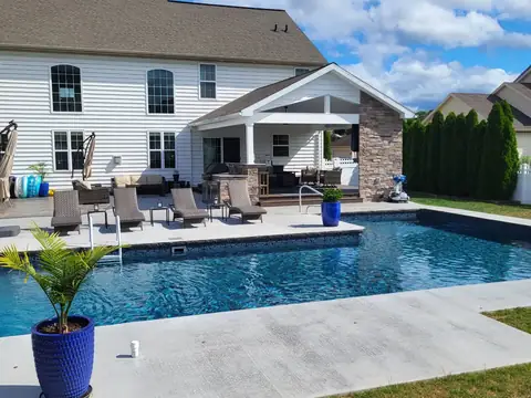 Covered patio by a pool with a stone column and an outdoor kitchen
