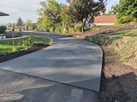 Finished curved concrete driveway between a lawn and a planted slope
