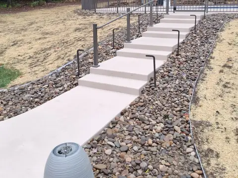 Concrete steps and a walk with a metal handrail, edged in river rock