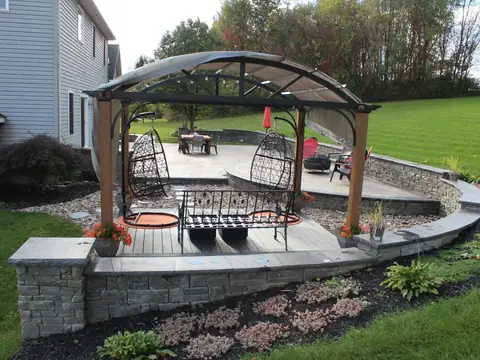 Pergola with a fabric roof over a low deck, set into a paver patio with seat walls