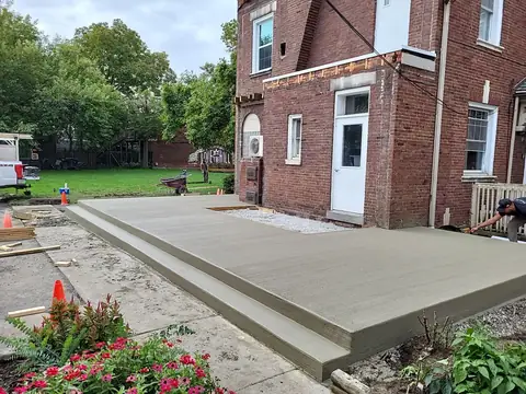 New concrete slab with a step beside a brick building and orange cones