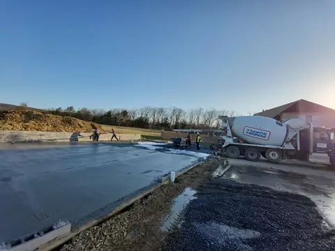 Crew pouring a large concrete slab beside a concrete mixer truck