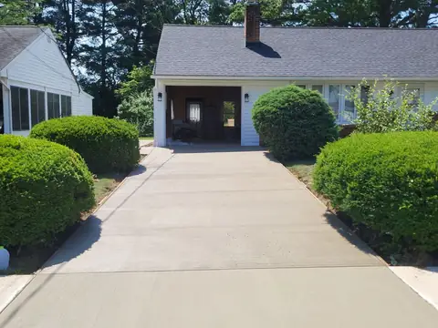 Concrete driveway with control joints leading to a garage between round shrubs