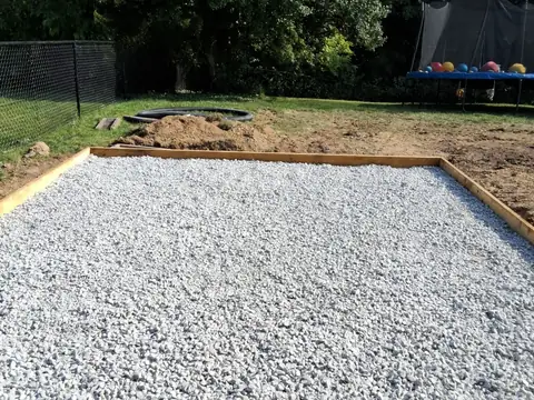 Crushed gravel base inside wood forms in a grassy backyard