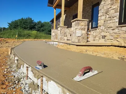 Freshly poured concrete walkway with two hand floats beside a stone house front