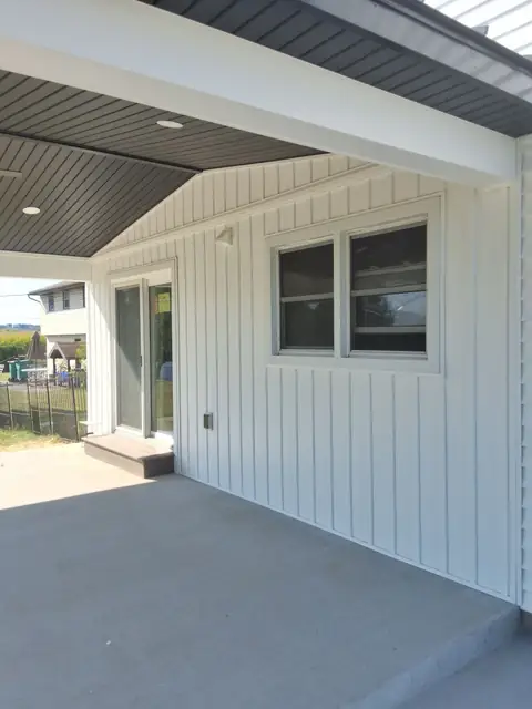 Concrete patio under a cover, beside white vertical siding