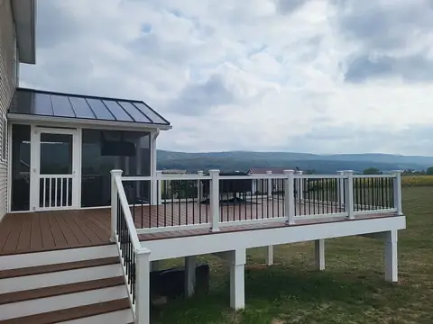 Deck with white railing and stairs, joined to a screened porch with a metal roof