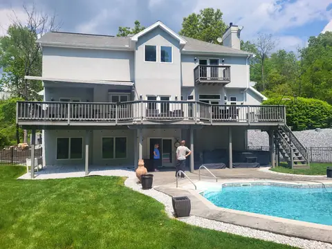 Large raised deck with stairs across the back of a house above a pool