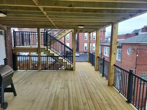 Lower level of a covered wood deck, with stairs and black railing