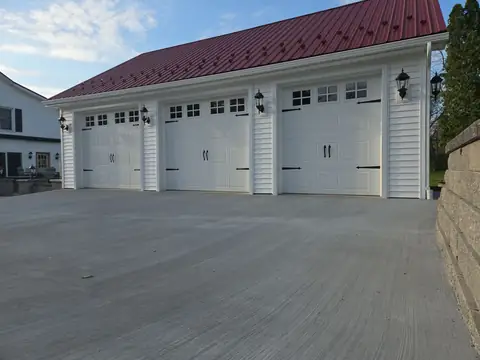 Concrete driveway leading to a three-car garage with a red metal roof