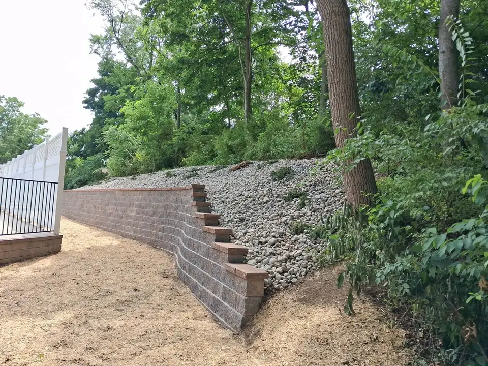 Curved block retaining wall on a sloped yard with river rock above